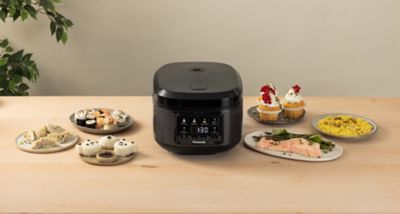 Леко повдигнат изглед отпред на уреда за готвене на ориз SR-DA152KXE в черно с различни приготвени ястия, подредени около него.