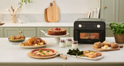 Фритюрник Panasonic Flex Air Fryer NF-BC1000 на кухненски плот с различни приготвени ястия.