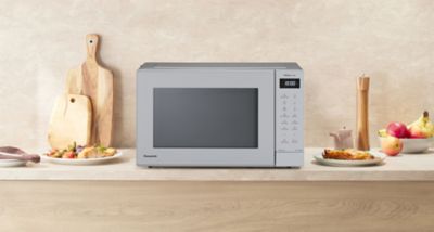 Panasonic GT66 microwave in silver on a kitchen counter, with cutting boards, a pepper mill, fruits, and plates of food in the background.