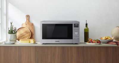 Panasonic CD58-mikrobølgeovnen i rustfritt stål er plassert på en kjøkkenbenk, med skjærefjøler, brød, en oljeflaske og en tallerken med mat arrangert rundt den.