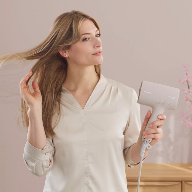 Imagine cu o femeie care își usucă părul folosind Panasonic Nanocare EH-NA0L în nuanța roz sakura