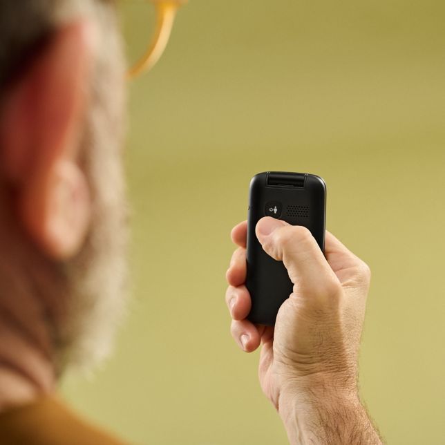 Mężczyzna pokazuje tył telefonu Panasonic K‌X-T‌U410 z przyciskiem alarmowym na zielonym tle.