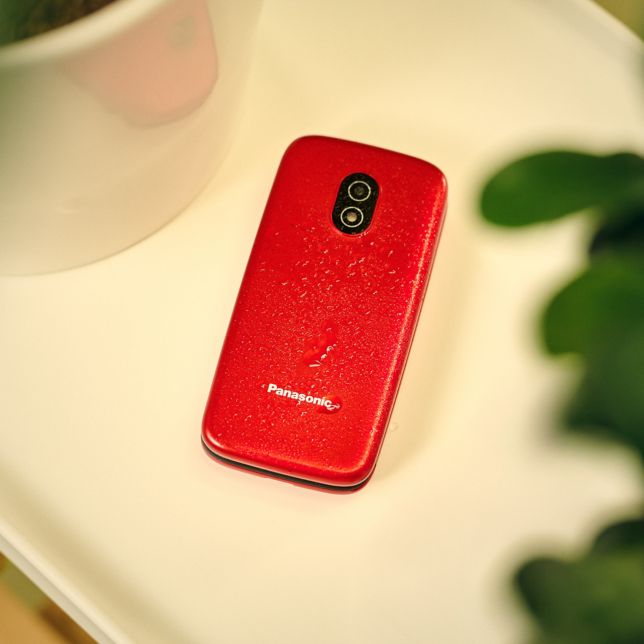 Czerwony Panasonic K‌X-T‌U410 leży obok rośliny, a na telefonie znajdują się krople wody, które mają świadczyć o jego
