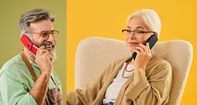 Two seniors on a colourful yellow-green background hold Panasonic KX-TU410 phones (black and red) to their ears.