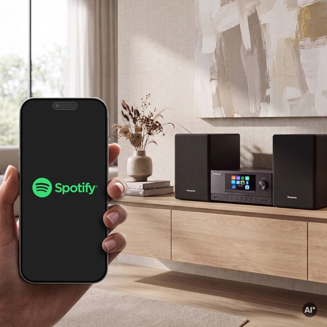 Egy kéz, amely egy Spotify logóval ellátott okostelefont tart egy fa tálalószekrényen egy Panasonic SC-PMX112 mellett, amely a Spotify Connect vezérlését illusztrálja.